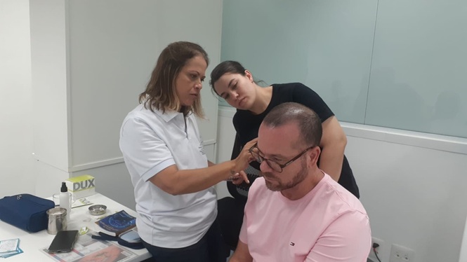 Foto horizontal: duas profissionais de saúde realizam atendimento em homem sentado, durante atividade do programa Saúde Itinerante.