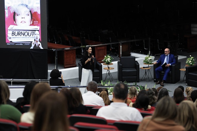 Izabella Camargo, de preto e branco, fala ao público; André Dacol, de azul, está sentado ao lado diante do público e telão, plenário do TJSC, evento sobre saúde mental, apresentando tema em preto, azul e branco