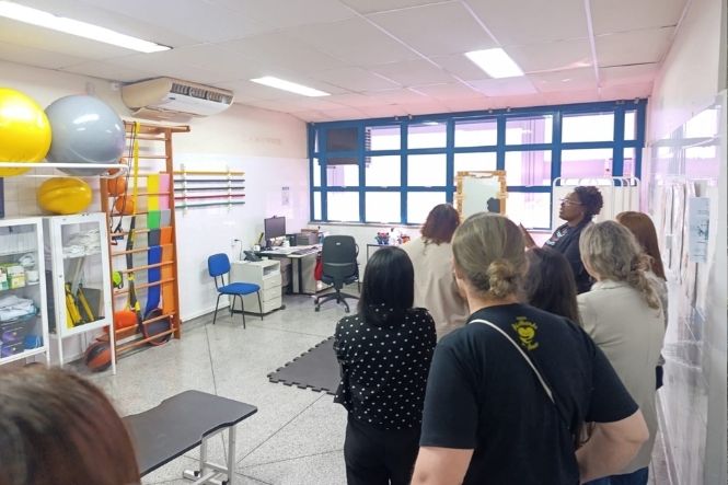 Foto horizontal: grupo de mulheres visita sala de atendimento do Sest Senat, com equipamentos e materiais de saúde no ambiente.