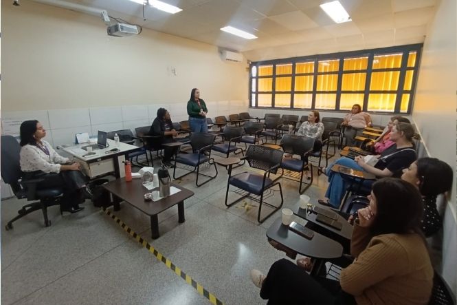 Foto horizontal: mulher em pé conversa com grupo de mulheres sentadas em sala de aula, durante atividade no Sest Senat.