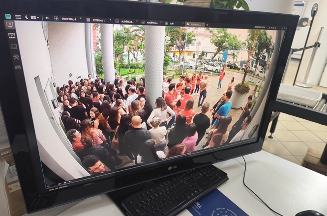 Foto horizontal: monitor de segurança exibe servidores e brigadistas reunidos na área externa do Fórum de Itajaí.