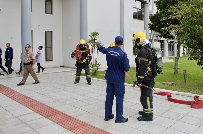 Foto horizontal: bombeiros militares e brigadistas coordenam simulado de combate a incêndio nas dependências do Tribunal de Justiça de Santa Catarina, durante treinamento de resposta a emergências.