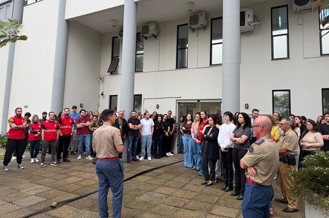 Foto horizontal: servidores, brigadistas de vermelho e bombeiros recebem orientações em frente ao Fórum de Itajaí.