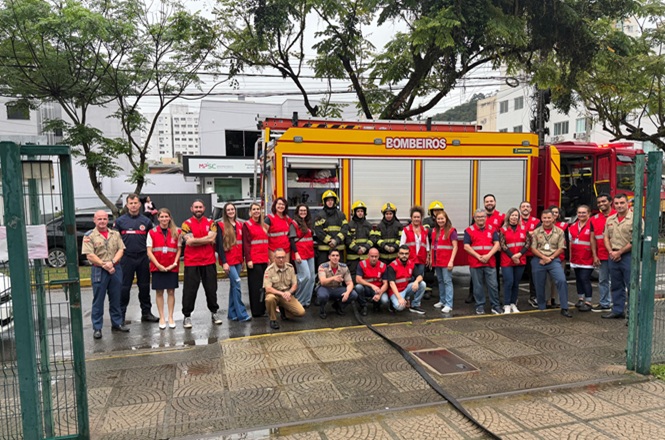 Foto horizontal: brigadistas de vermelho e bombeiros posam diante de caminhão de resgate após simulado no Fórum de Itajaí.