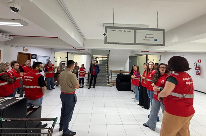 Foto horizontal: brigadistas com coletes vermelhos recebem orientações durante simulado de emergência no Fórum de Itajaí.