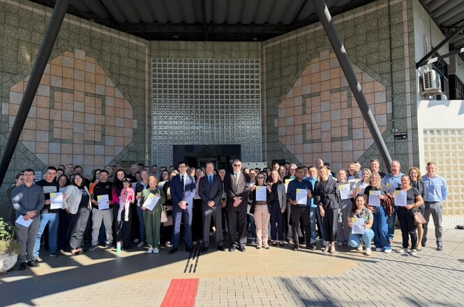 Foto horizontal: Beneficiários e autoridades reúnem-se em frente ao fórum após a entrega de recursos do programa PJSC Mais Social.