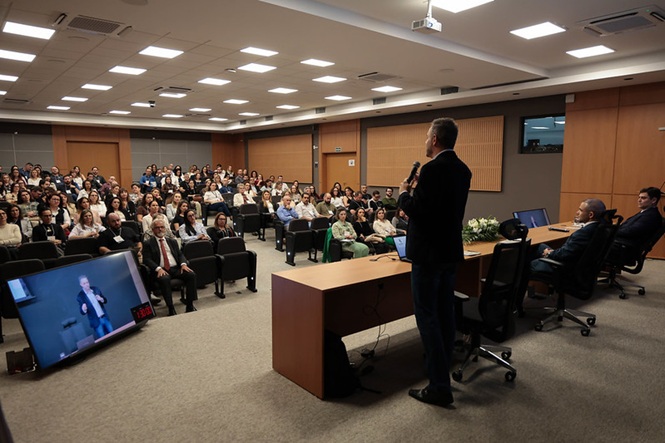 Foto horizontal: chefe da Divisão de Desenvolvimento e Valorização de Pessoas da DGP, Marcelo Dias e Silva, fala ao microfone diante do público em auditório.
