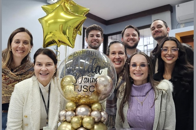Foto horizontal: servidora celebra 30 anos de atuação no TJSC ao lado de colegas e de decoração comemorativa.