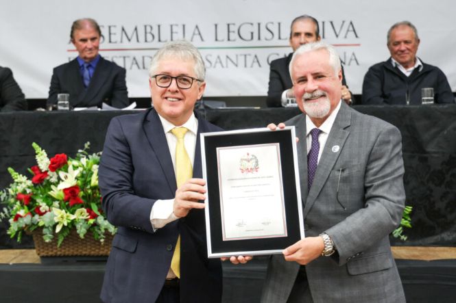 Foto horizontal: autoridades exibem certificado durante cerimônia na Assembleia Legislativa, registro de homenagem oficial, ambiente institucional, clima solene.