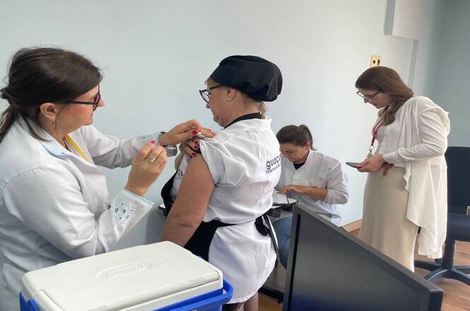 Profissional de saúde aplica vacina em servidora durante campanha de imunização no ambiente de trabalho.