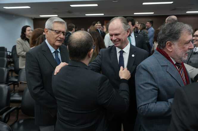 Foto horizontal: desembargador Rubens Schulz cumprimenta participante com a mão no ombro, interação próxima entre autoridades, ambiente institucional, clima cordial.