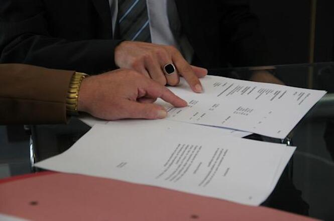 Foto horizontal: mãos apontam documento sobre mesa, análise de informações em andamento, clima de decisão e formalização.