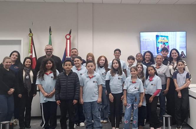 Foto horizontal: estudantes, professores e servidores posam em sala de audiências após visita educativa ao fórum, durante atividade de aproximação com o Poder Judiciário.