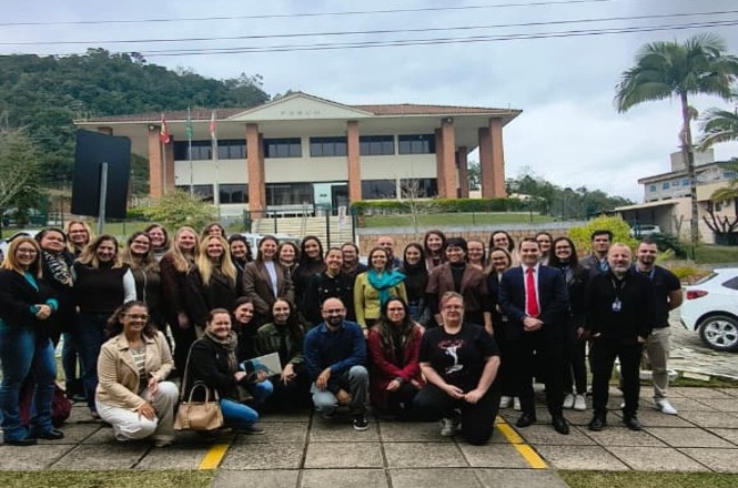 Foto horizontal: Participantes de capacitação reúnem-se para foto oficial em frente ao fórum após o encerramento das atividades.