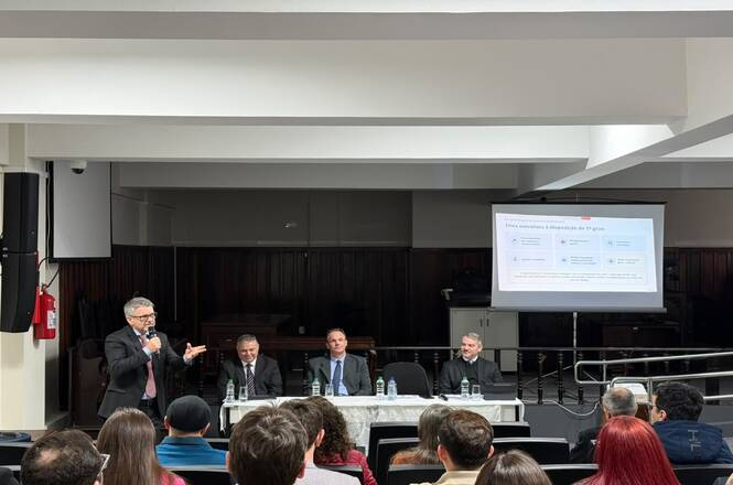 Foto horizontal: desembargador Dinart Francisco Machado fala ao microfone diante do público em auditório.