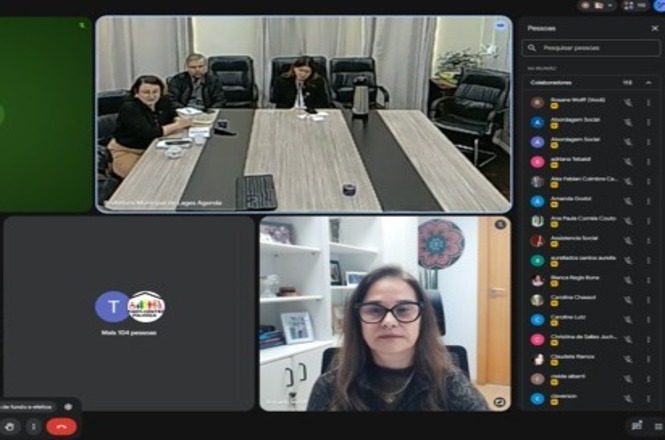 Imagem horizontal mostra reunião virtual com autoridades em sala e participante conectada por videochamada.