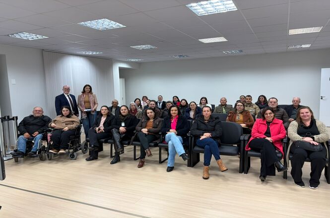 Foto horizontal: participantes acompanham encontro na comarca de Xanxerê, reunidos em auditório.