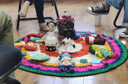 Pessoas sentadas em círculo, participando de uma dinâmica com objetos coloridos dispostos no chão.