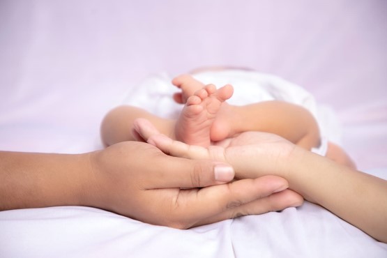 Imagem ilustrativa de duas mãos segurando pés de bebê.