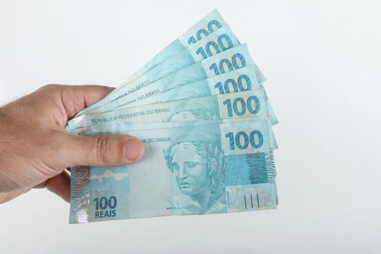 Mão segurando notas de cem reais.