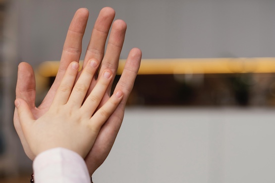 Mão de criança apoiada em mão de adulto.
