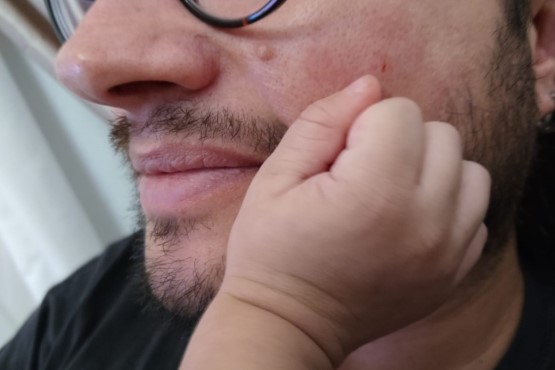 Mão de bebê apoiada em rosto de homem.