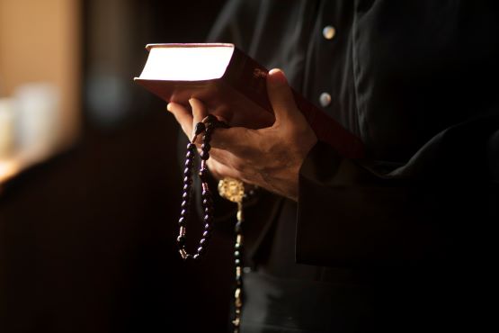 Padre segurando bíblia e rosário.