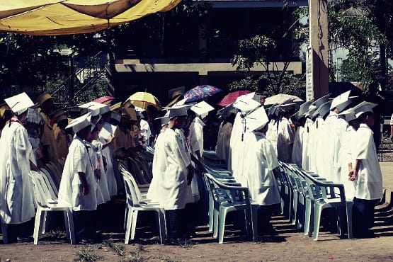 Crianças vestidas de beca e chapéu de formatura.