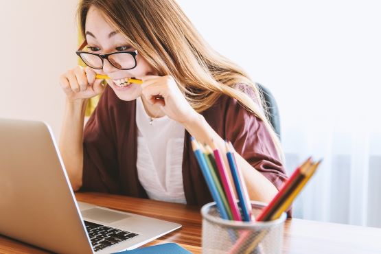 Mulher mordendo lápis e olhando o computador.