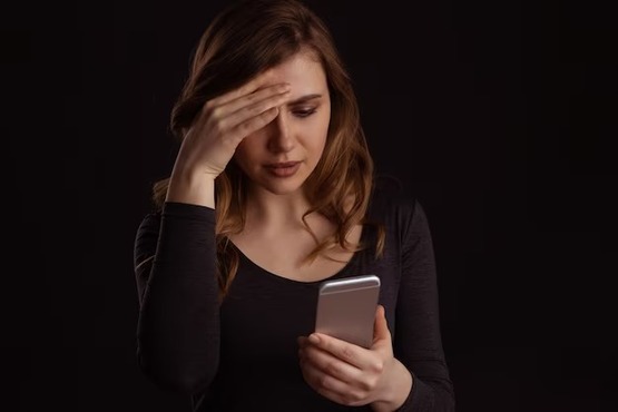 Mulher com a mão na cabeça usando celular.