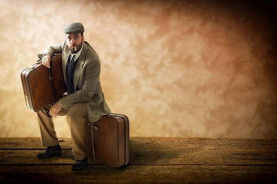 Homem sentado em mala enquanto segura outra mala