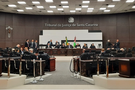 Foto colorida: plenário com magistrados e público, Tribunal de Justiça, sessão judicial, deliberando em madeira, cinza e verde