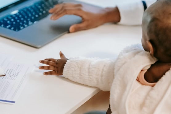 Bebê ao lado de mãe digitando em notebook