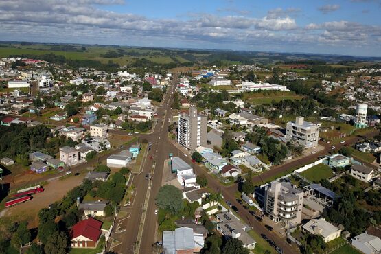 Uma imagem áerea de uma cidade, onde aparecem as ruas, as casas e muitos campos verdes.