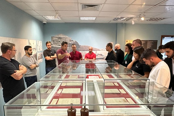 Visitantes do Museu do Judiciário em volta de cúpula de vidro quadrada olham para documentos históricos