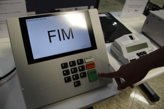 Em uma urna eletrônica, pessoa aperta a tecla da cor verde com a palavra “CONFIRMAR” escrita e aparece “FIM” no visor do aparelho.