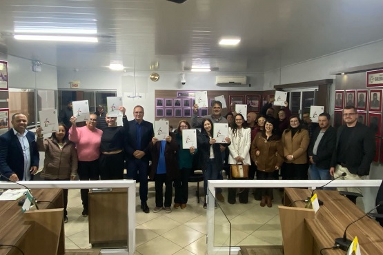 Pessoas lado a lado exibindo seus títulos de propriedade dentro de sala pequena.