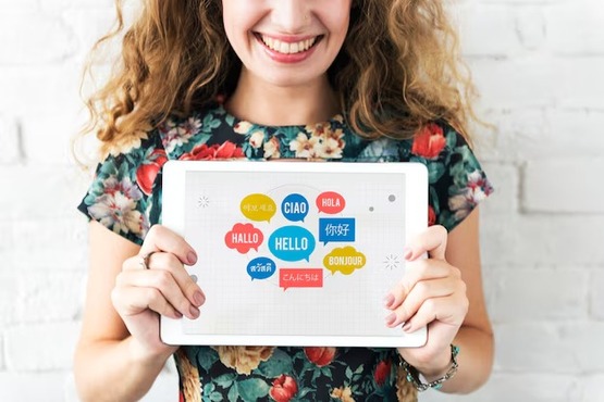 Imagem de uma jovem segurando um quadro com várias palavras escritas em diferentes idiomas dentro de balões nas cores amarelo, vermelho e azul claro e escuro.