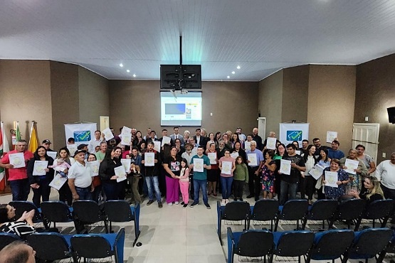 Em frente de um palco, pessoas seguram papéis e posam para foto.