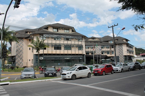 Fachada do fórum de Joinville vista de um ângulo mais a esquerda e com carros estacionados na frente. A edificação tem quatro andares.