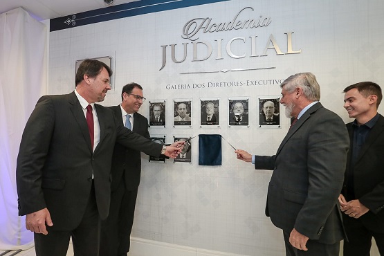 A foto de Luiz Antônio Zanini Fornerolli está coberta por um tecido preto que está sendo retirado por 4 homens integrantes da Academia Judicial.