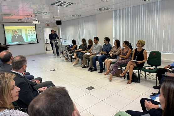 Grupo de pessoas sentadas em cadeiras colocadas em circulo e um homem em pé, junto a um projetor.