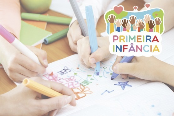 Papel sob a mesa sendo desenhado por mãos de crianças com  canetas coloridas.