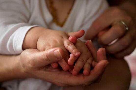 Mão de um homem, segurando as mãos de uma criança com aproximadamente um ano.