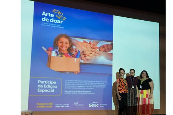 Três mulheres em frente a uma projeção escrita "arte de doar".