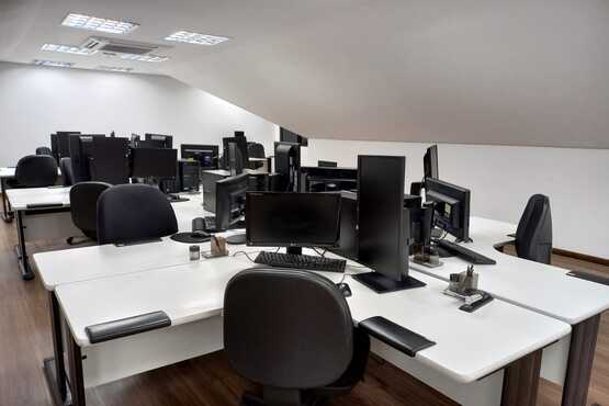 Sala vazia com mesas, cadeiras e computadores.
