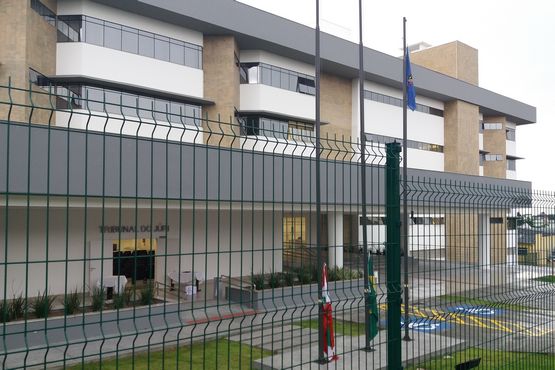 Lateral do prédio da comarca de Canoinhas, O prédio é cercado por grades e possui alguns mastros com bandeiras no interior do terreno.
