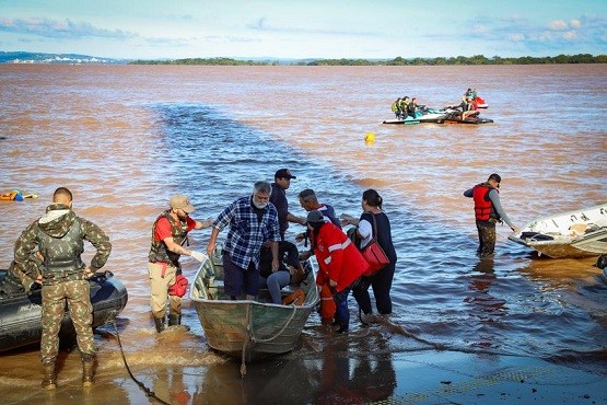 Pessoas descem de um bote em meio às enchentes.