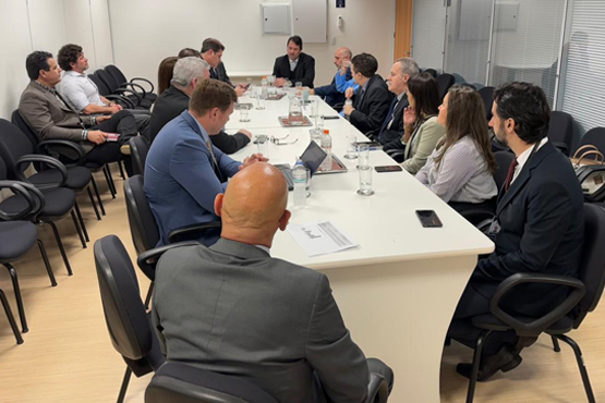 Foto tirada de pessoas sentadas em cadeiras estofadas pretas ao redor de uma mesa branca.