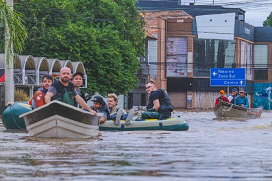 Foto tirada de três botes com homens dentro. Eles navegam nas enchentes do Rio Grande do Sul.